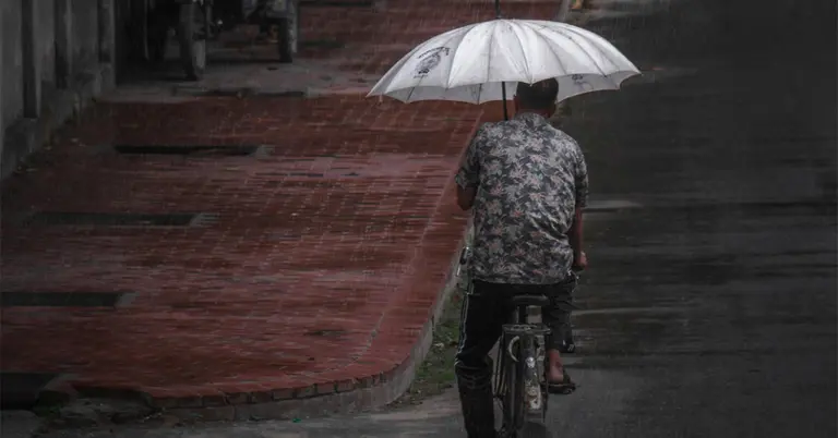 বৃষ্টিতে ছাতা মাথায় একজন সাইকেল আরোহী